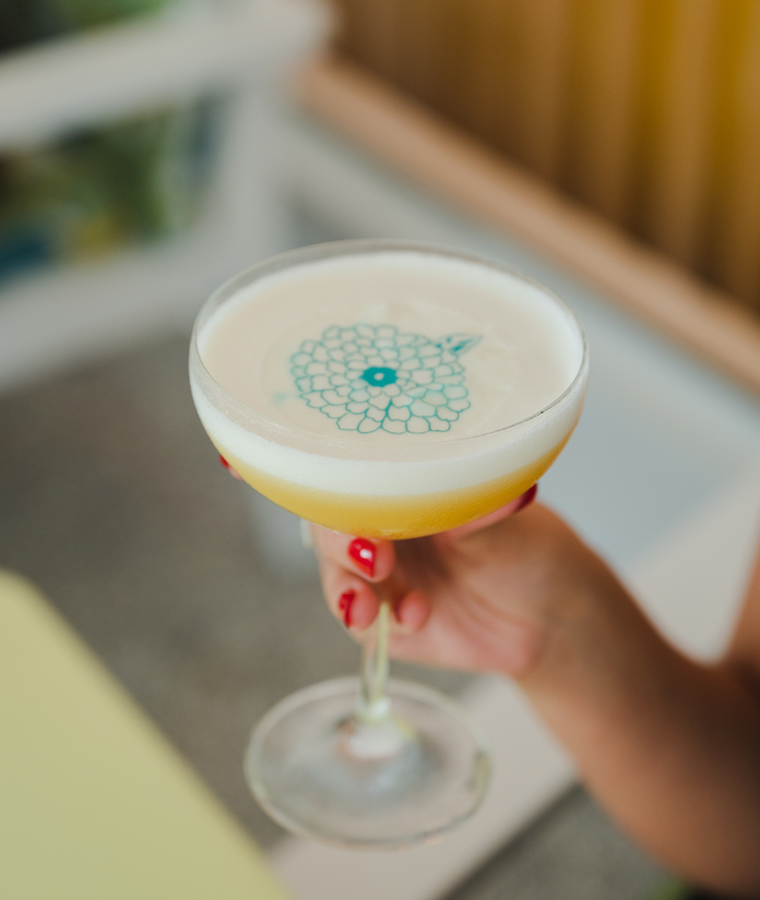 A refreshing green drink with ice, garnished with mint and lemon slice, served in a tall glass on a patterned floral tablecloth.