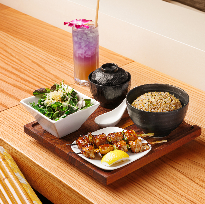 Modern outdoor dining area with lush greenery, white chairs, and a "MAKOTO" sign.