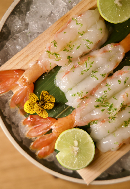 Person holds chopsticks lifting steaming noodles with purple cabbage coleslaw in a stone bowl.