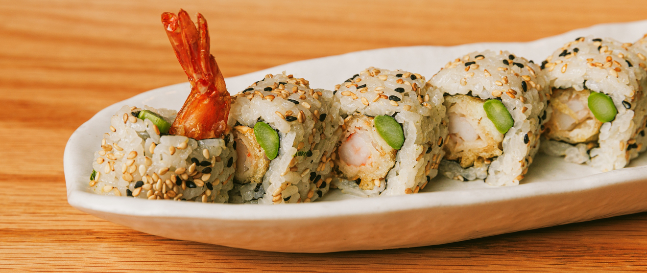 A beautifully presented sushi roll garnished with a shrimp and sesame seeds on a white plate.