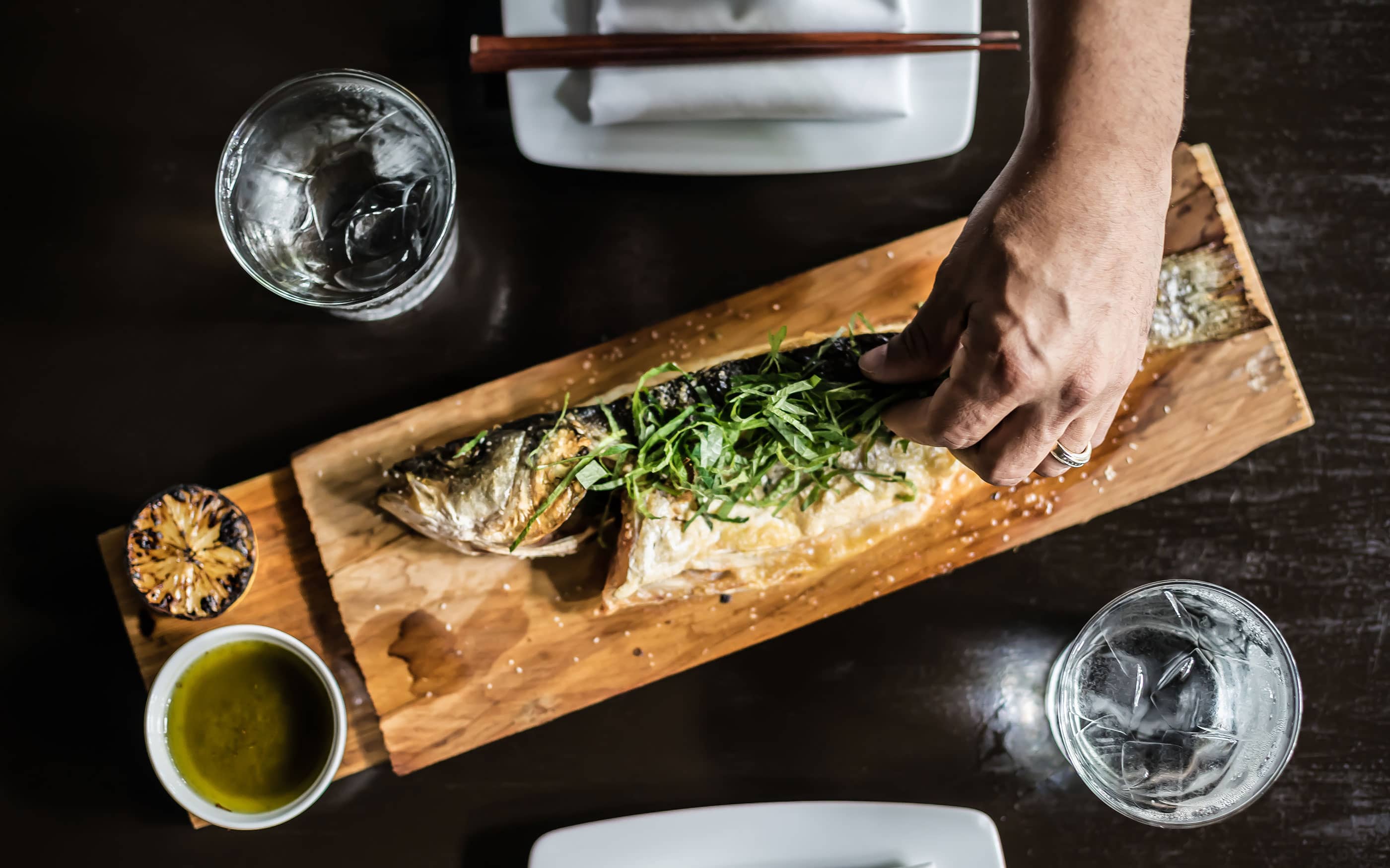Table view from above of hand garnishing fish with green onions served on wood board